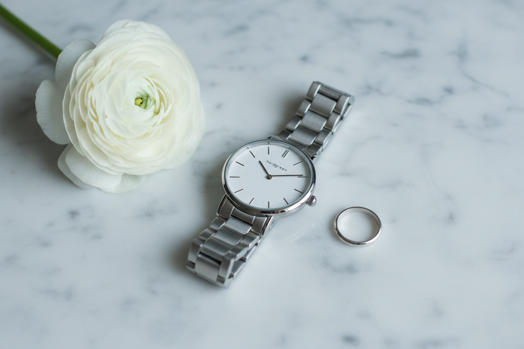 Nordgreen Native 32mm Silver 3-Link Dress Watch flat lay on white marble with white ranunculus